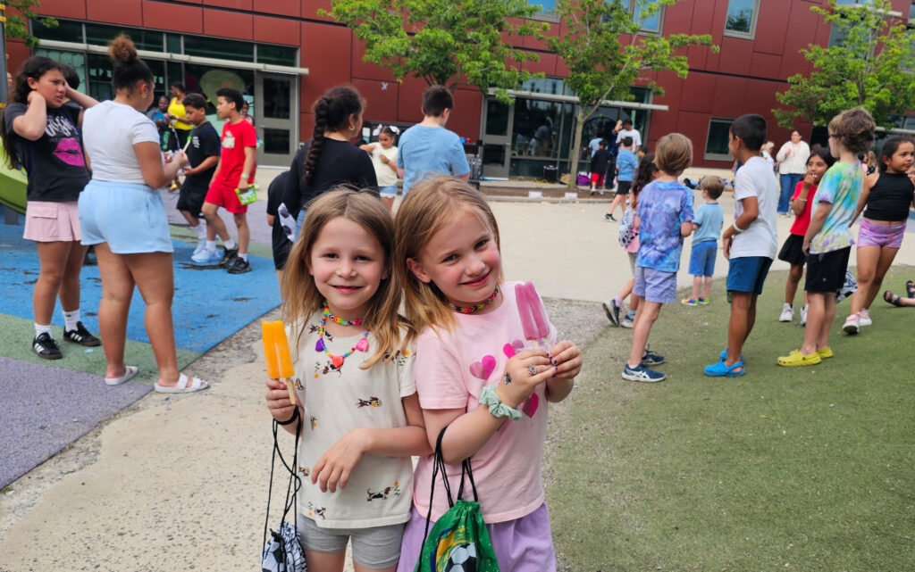 two girls pose outside their school with popsicles
